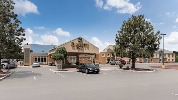 A Quality Inn hotel with a parking lot, a black car in the foreground, and a clear blue sky.