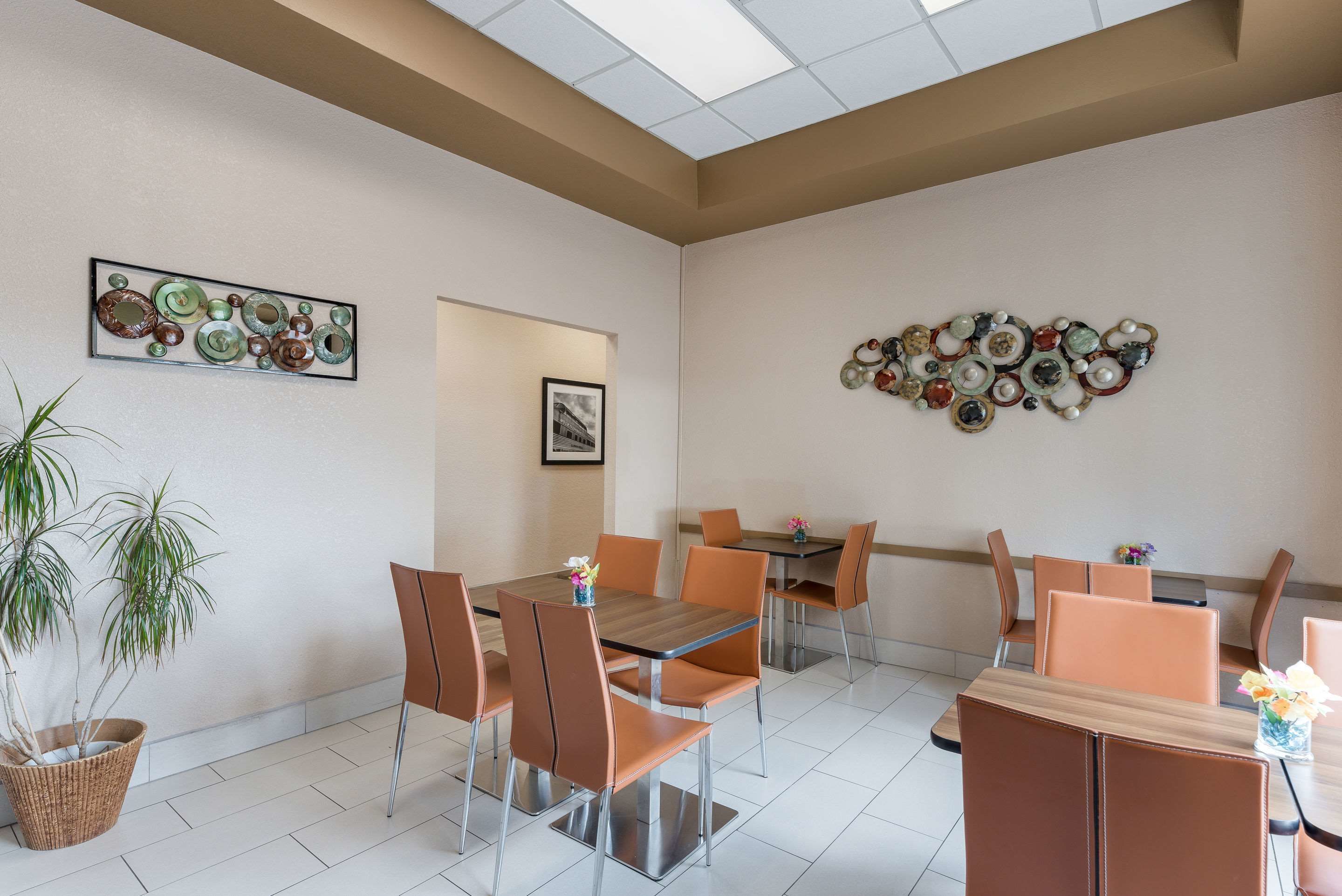 A dining area with a wooden table and brown chairs, a potted plant, and decorative wall art.