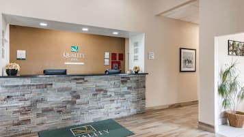 A reception area with a stone counter, a green doormat, and a wall-mounted sign for Quality Inn.