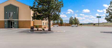 A parking lot with a building on the left, a tree in the center, and a clear sky.