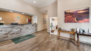 A reception area with a stone counter, a framed picture of a canyon, and a wooden desk with a plant.