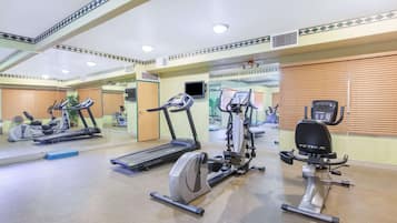 Un gimnasio con diversas máquinas de ejercicio, incluyendo cintas de correr y bicicletas estáticas, y un espejo que refleja el equipo.