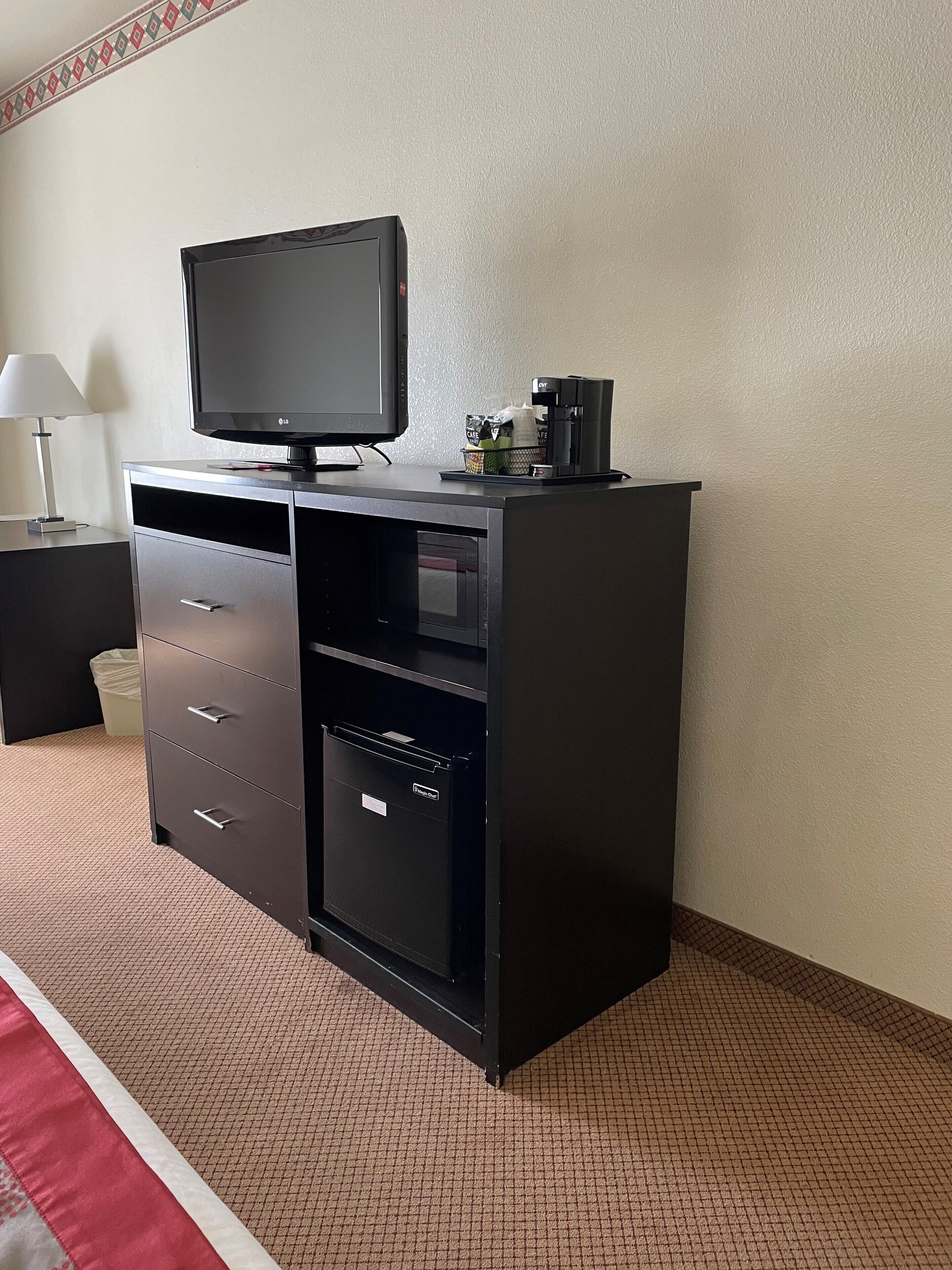 A hotel room with a black entertainment center, a flat-screen TV, a coffee maker, and a trash bin.