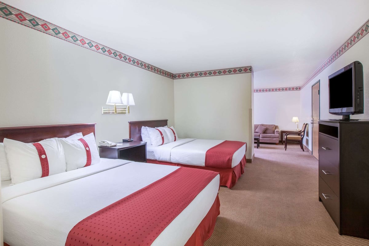 A hotel room with two beds, a TV, a desk, and a chair.