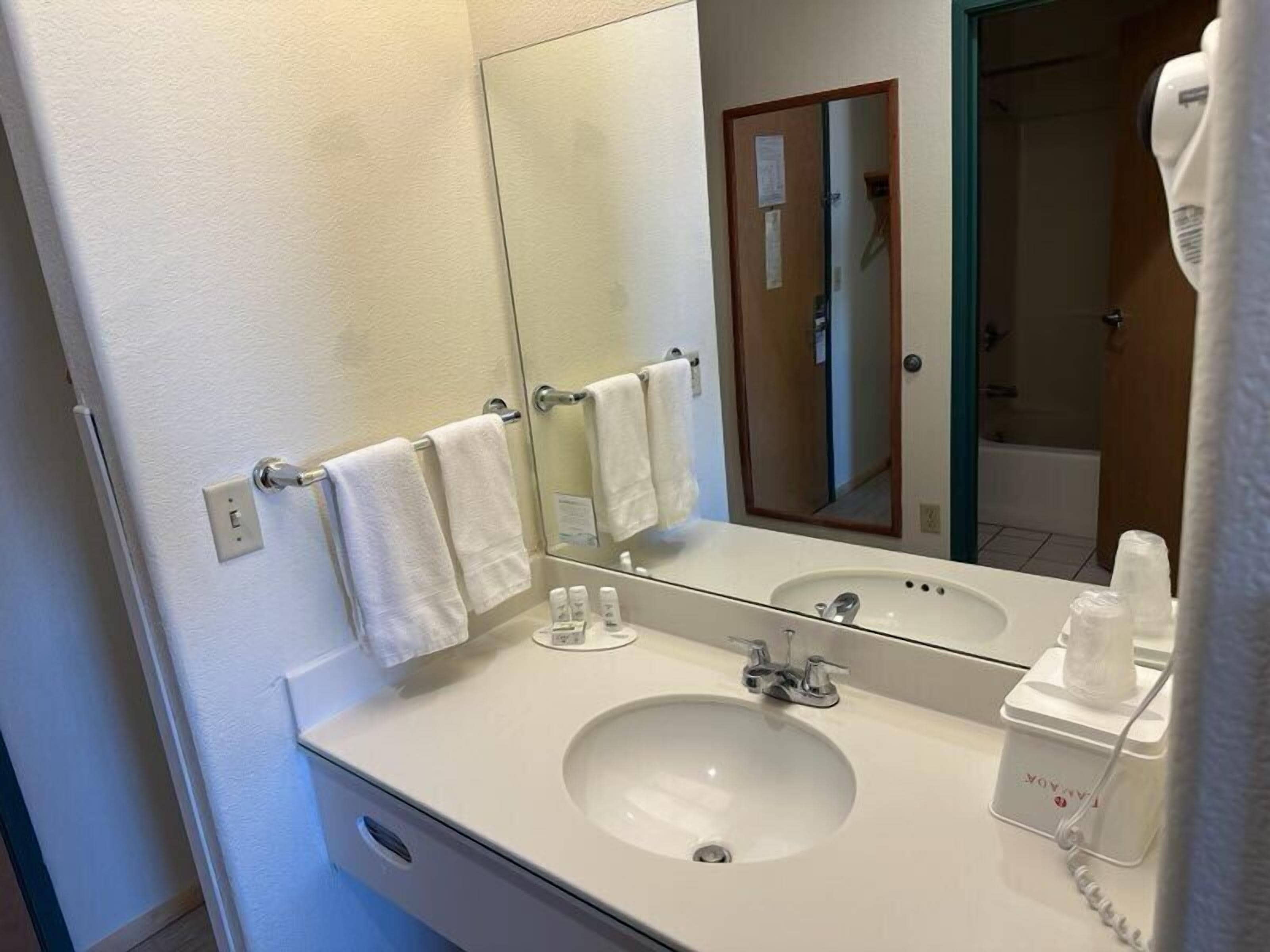 Un baño de hotel con un lavabo blanco, un espejo y un perchero con tres toallas.