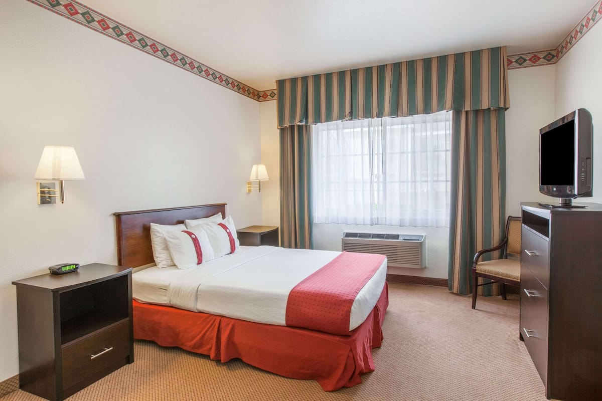 A hotel room with a bed, bedside tables, a desk, a television, and a window with curtains.