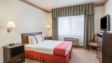 A hotel room with a bed, bedside tables, a desk, a television, and a window with curtains.