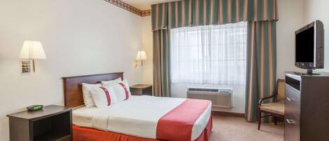 A hotel room with a bed, bedside tables, a desk, a television, and a window with curtains.
