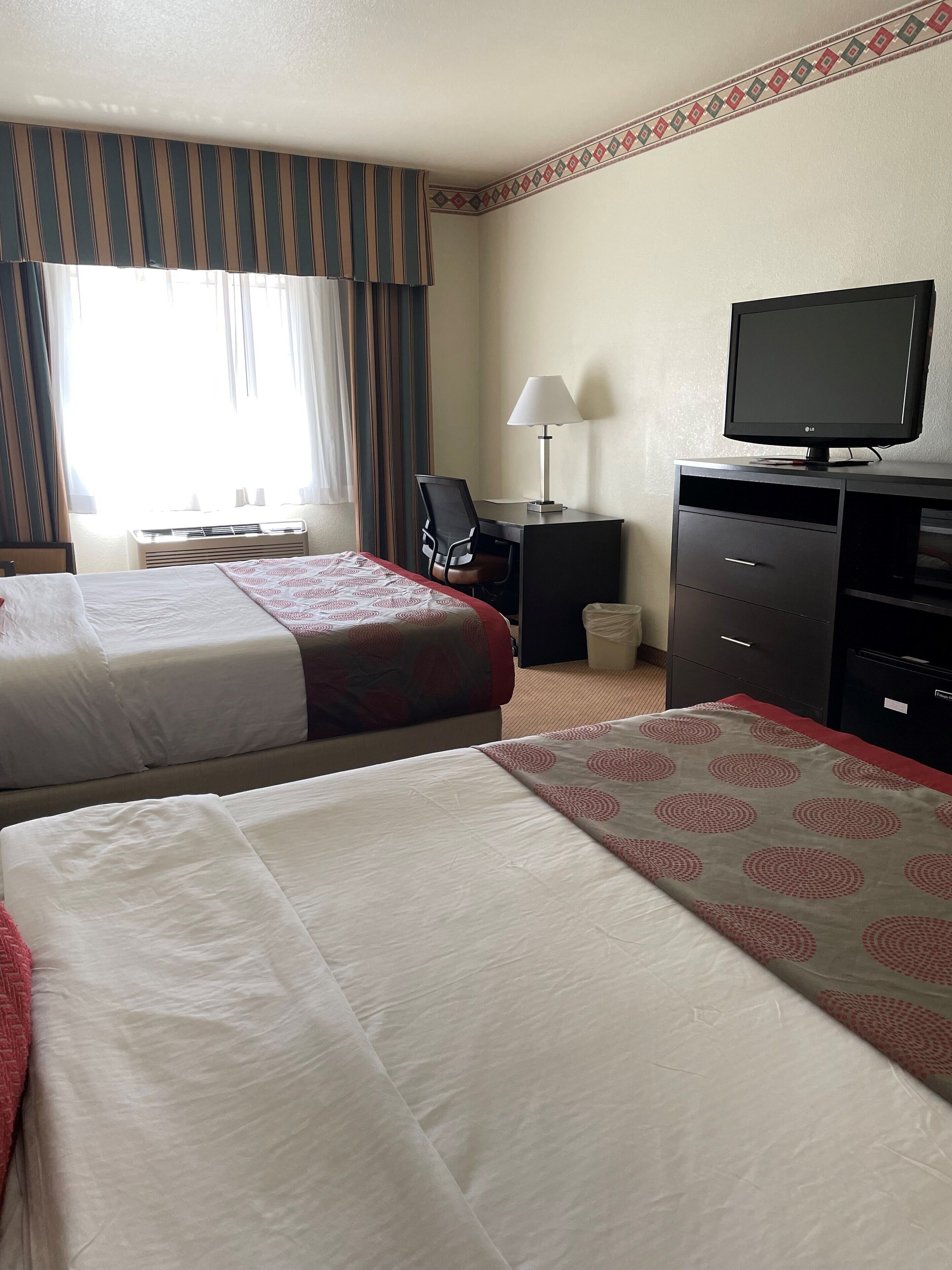 A hotel room with two beds, a desk with a chair, a television, and a lamp.