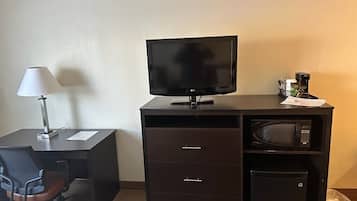 Habitación de hotel con escritorio, una silla, televisor, microondas y un cesto de basura.