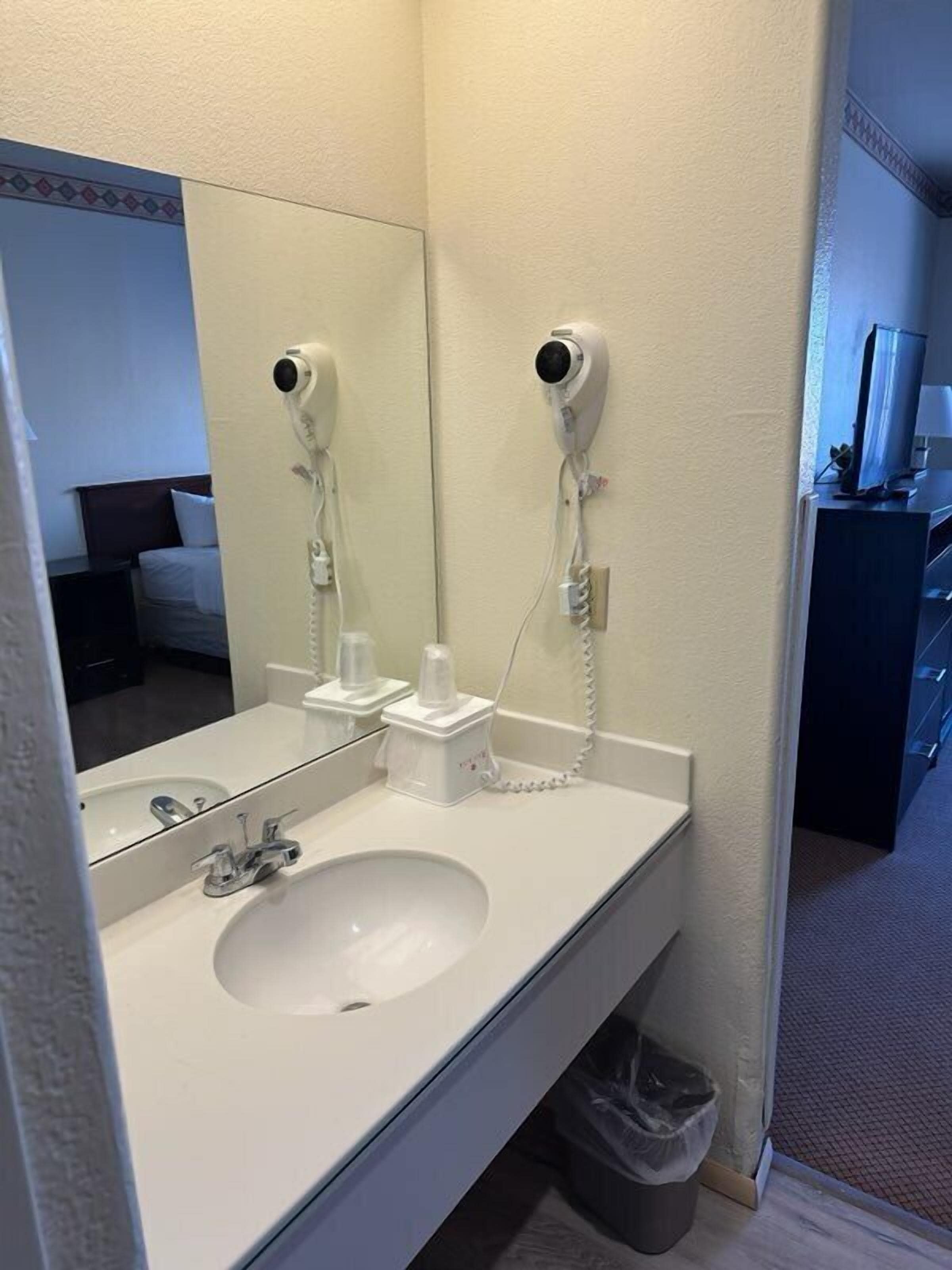 Ein Hotelbadezimmer mit einem großen Spiegel, einem Waschbecken und zwei an der Wand befestigten Haartrocknern.