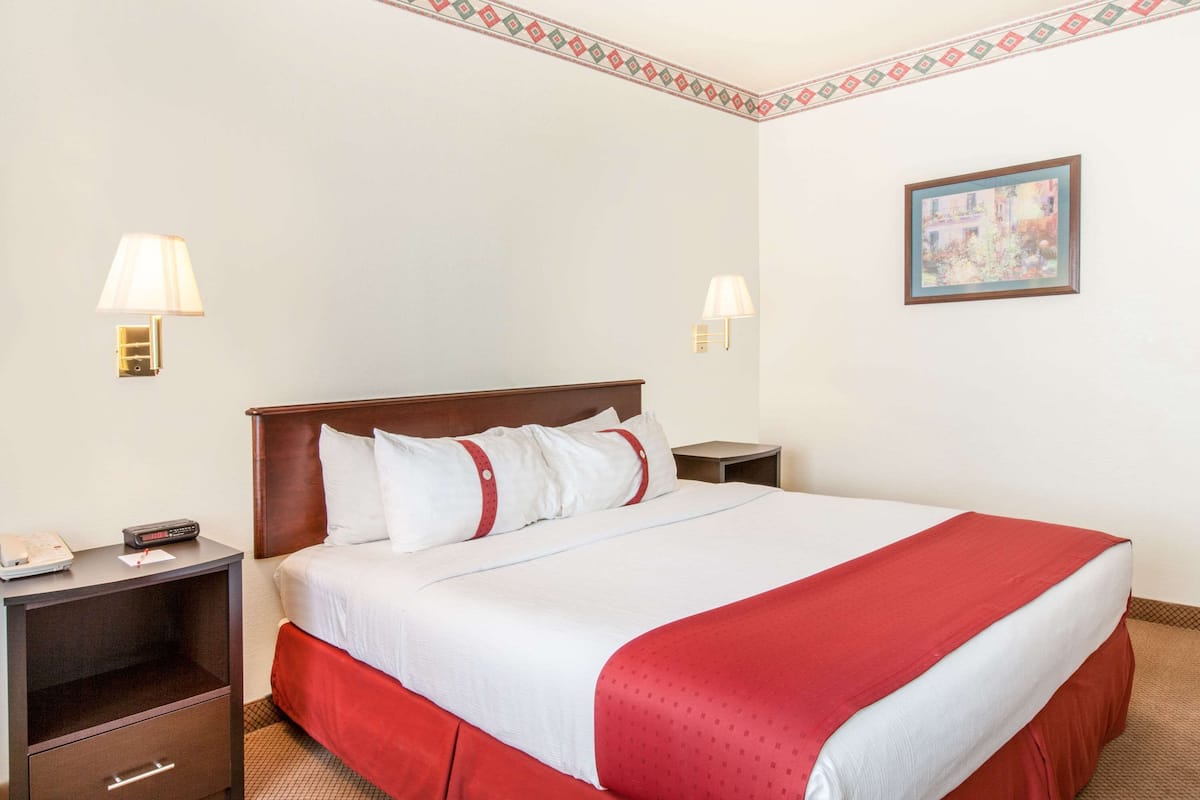 A hotel room with a large bed, two bedside tables, a nightstand, a lamp, and a framed picture on the wall.