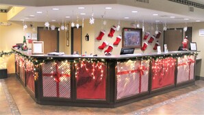 A reception desk with Christmas decorations, including stockings and snowflakes, and a monitor above it. - Ramada by Wyndham Williams/Grand Canyon Area (Williams)