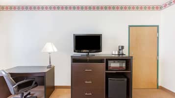Habitación de hotel con escritorio, silla, televisor, cafetera, microondas y una puerta.