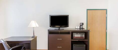 A hotel room with a desk, chair, television, coffee maker, microwave, and a door.