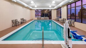 An indoor swimming pool with clear glass walls, multiple seating areas, and a view of the sunset through large windows. - Hampton Inn Denver-International Airport (Denver)