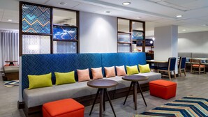 A modern hotel lobby with a blue patterned sofa, orange ottomans, and a patterned rug. - Hampton Inn Denver-International Airport (Denver)