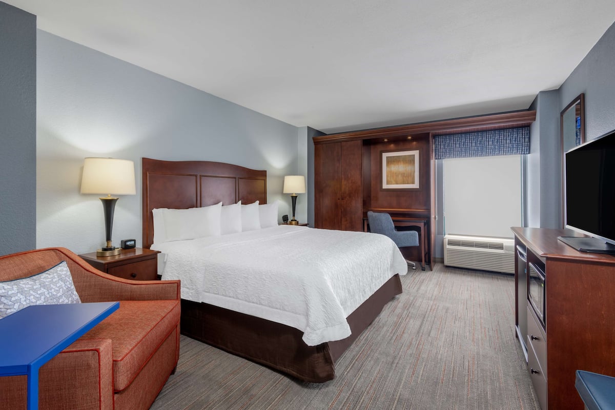 A hotel room with a large bed, a desk, a TV, and a sofa.