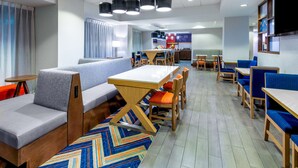 A modern hotel lobby with seating areas, a dining space, and a kitchen in the background. - Hampton Inn Denver-International Airport (Denver)
