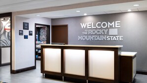 A reception desk with a "Welcome to the Rocky Mountain State" sign, a framed picture, and a "Treats" sign on the wall. - Hampton Inn Denver-International Airport (Denver)