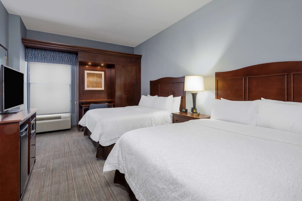 A hotel room with two beds, a television on a dresser, and a desk with a lamp.
