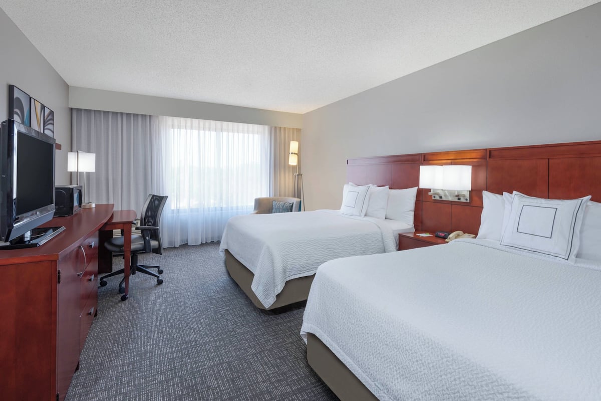A hotel room with two beds, a desk with a computer, a TV, and a chair.