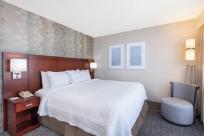 A hotel room with a large bed, a wooden headboard, two bedside lamps, a nightstand, a chair, and two framed pictures on the wall. - Courtyard by Marriott Harlingen (Harlingen)