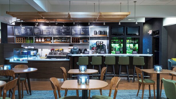 Un área de bar moderna con diversas opciones de asientos, una máquina de café y un tablero de menú.