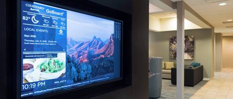 A digital display in a hotel lobby with a mountain view, a sofa, and a painting on the wall.