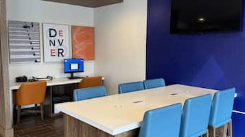 Una sala de conferencias con una gran mesa, sillas azules, una computadora y obras de arte en la pared.