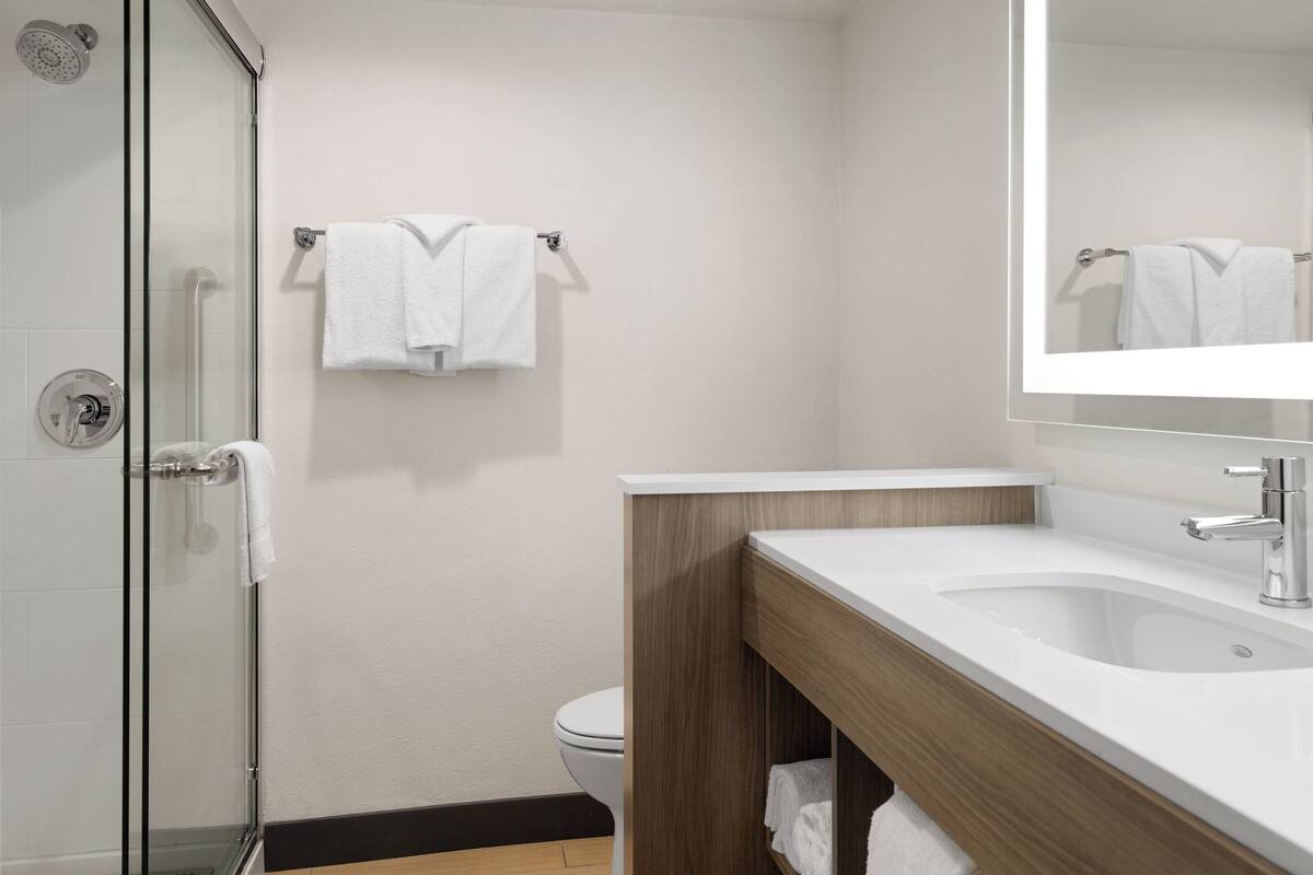 A modern bathroom with a glass shower enclosure, a white sink with a wooden vanity, and a towel rack with two towels.