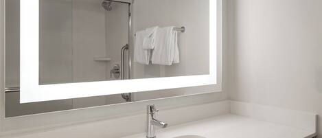 Une salle de bain moderne avec un grand miroir, un lavabo blanc et une douche.