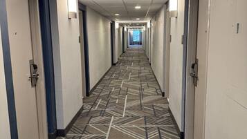 A hotel hallway with carpeted floors, doors on both sides, and overhead lighting.
