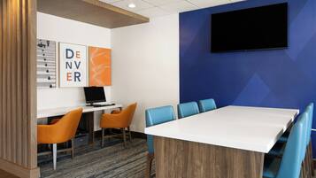 A conference room with a white table, blue chairs, a TV on the wall, and artwork on the wall.