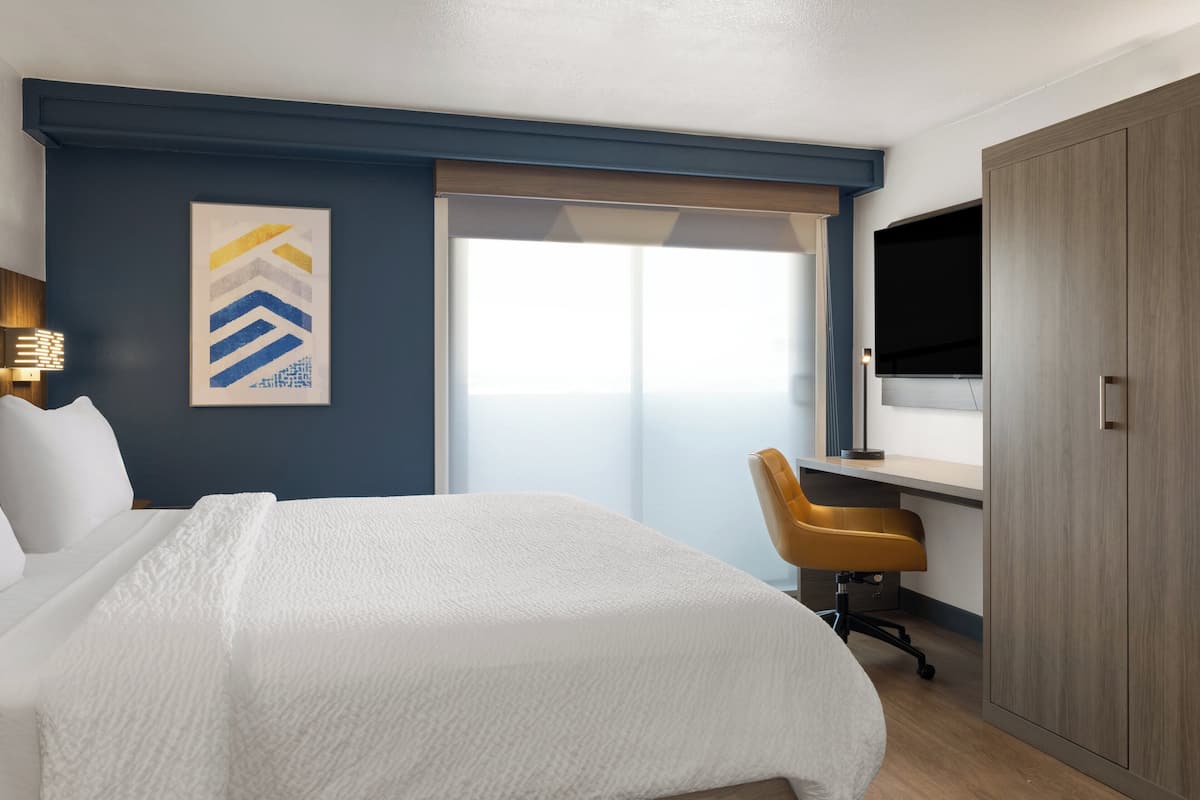 A hotel room with a bed, a desk, a chair, a TV, and a wardrobe.