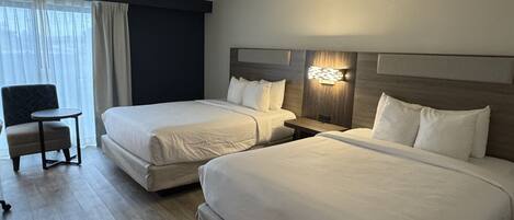 Une chambre d’hôtel avec deux lits simples, une petite table, une chaise et une grande fenêtre avec des rideaux.