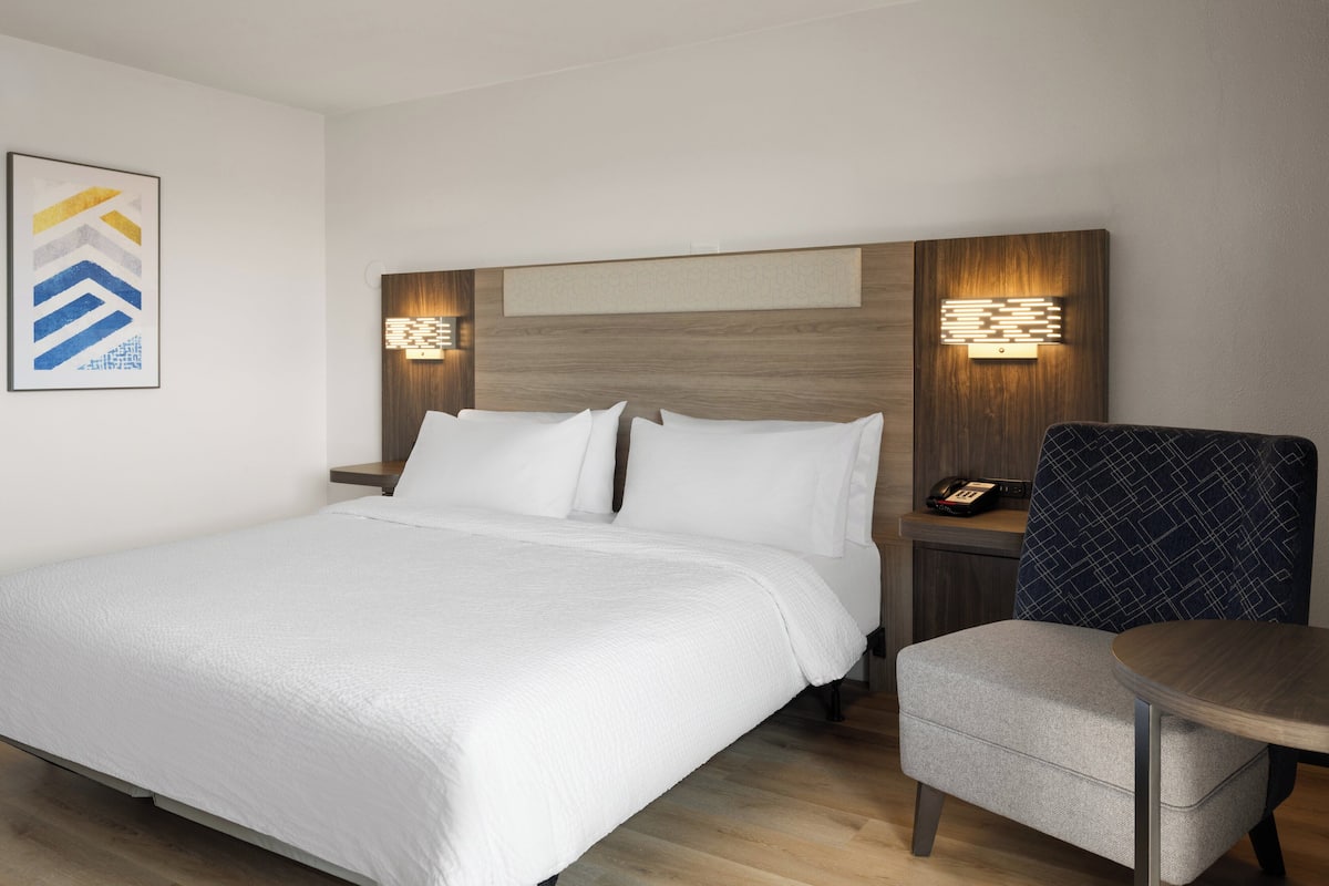 A hotel room with a large bed, a bedside table with a phone, and a chair.