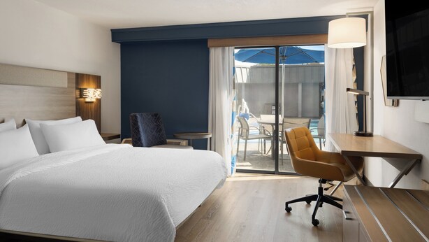 Habitación de hotel con una cama grande, un escritorio, una silla y vistas al patio exterior.