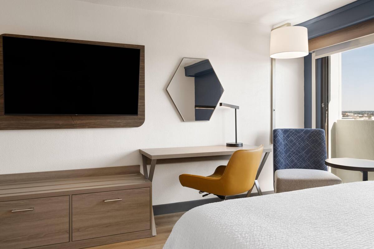 A hotel room with a bed, a desk, a chair, a TV, and a window.