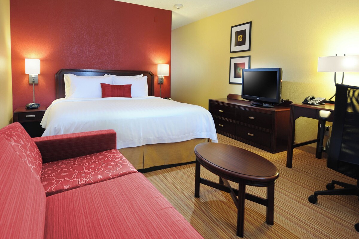 Habitación de hotel con cama, escritorio con computadora, televisor y sofá rojo.
