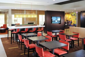 Ein modernes Restaurant mit mehreren Tischen und roten Stühlen, einer Bar und einer digitalen Speisekarte.