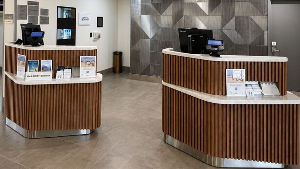 A hotel reception area with two reception desks, a wall-mounted screen, and a trash bin.