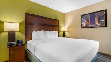 Habitación de hotel con una cama grande, cabecera de madera, mesita de noche con teléfono y reloj, y un cuadro en la pared que muestra un paisaje urbano.