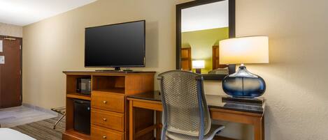 A hotel room with a bed, a desk with a computer, a television, a lamp, and a mirror.