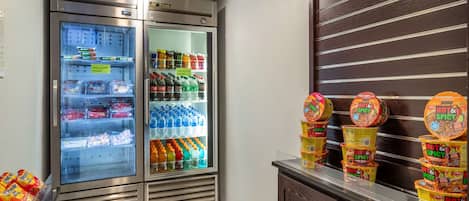 A vending machine with snacks and drinks, a refrigerator with beverages, and a display of hot sauce containers.