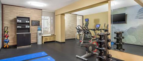 Une salle de sport équipée de matériel d’exercice, d’un distributeur d’eau et d’un panneau indiquant les équipements disponibles.