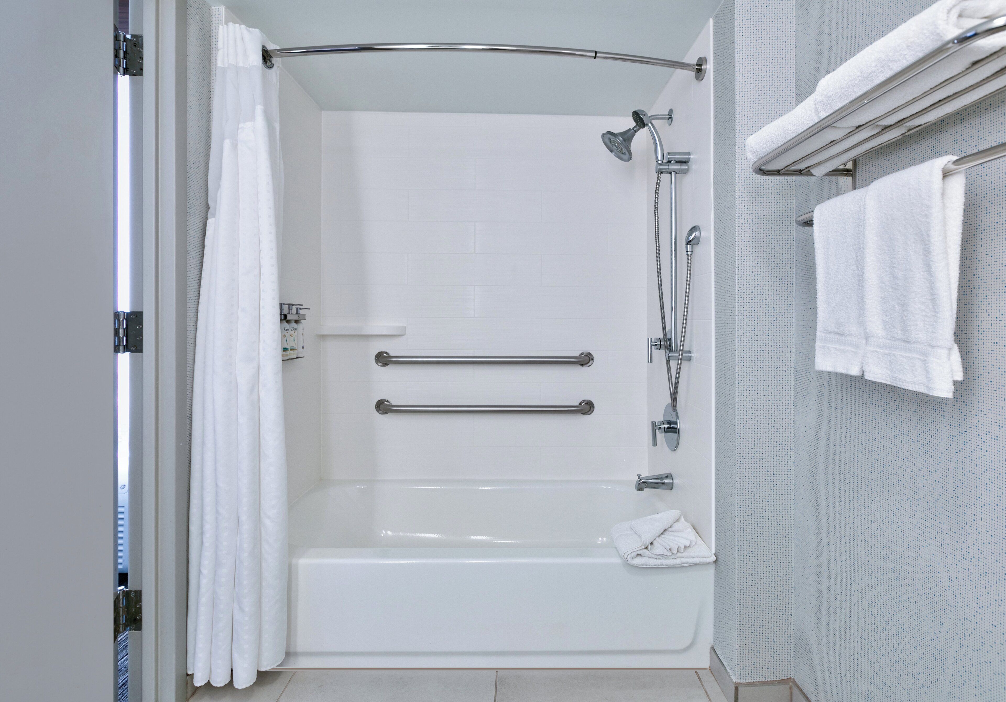 Une salle de bain moderne dotée d’une douche à l’italienne, de barres d’appui, d’un pommeau de douche amovible et d’un porte-serviettes.