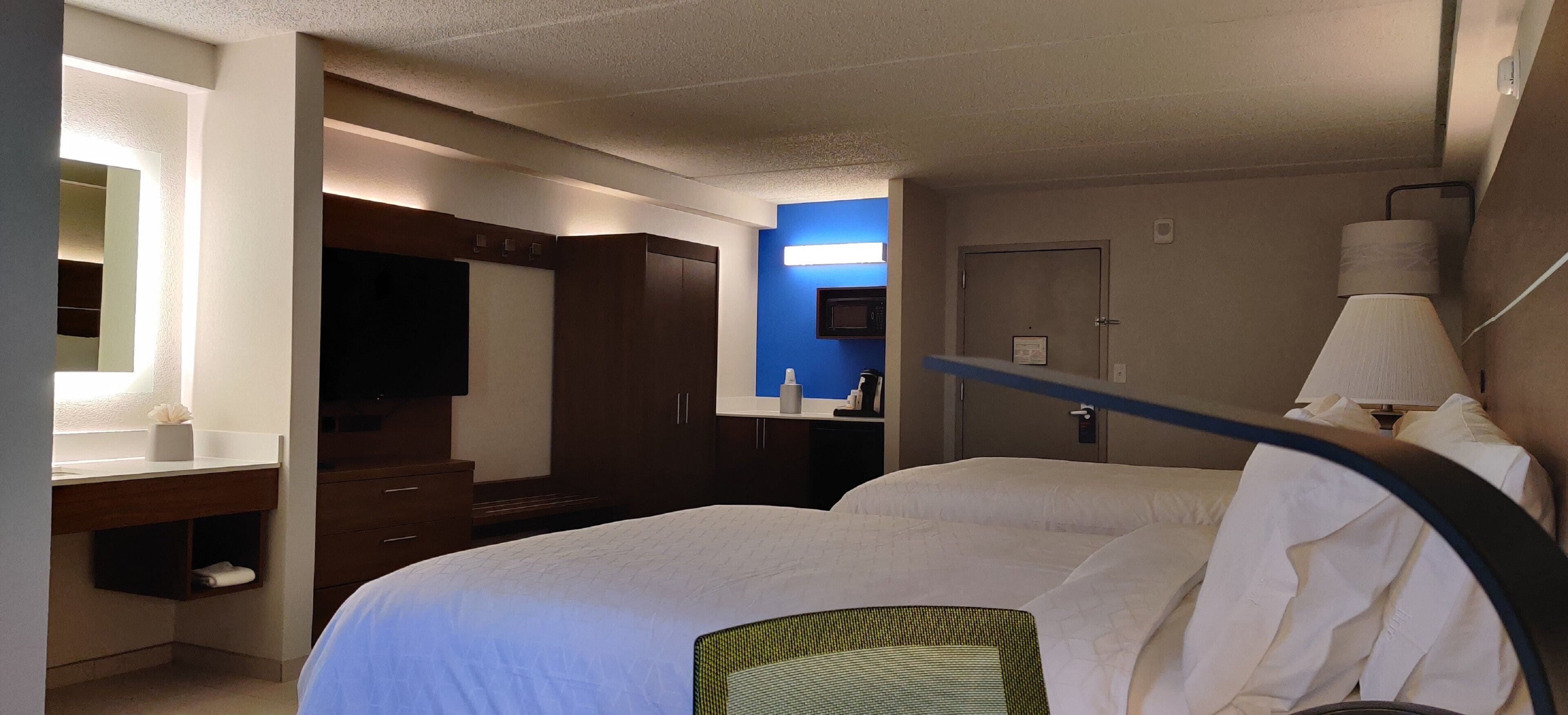 A hotel room with a bed, a desk, a television, a microwave, and a door.