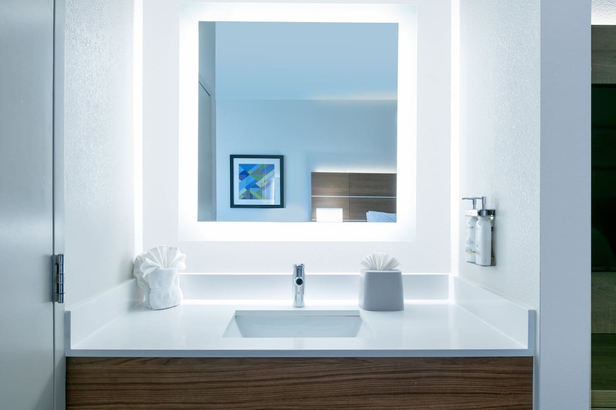 A modern bathroom with a white sink, a mirror, and a framed picture on the wall.