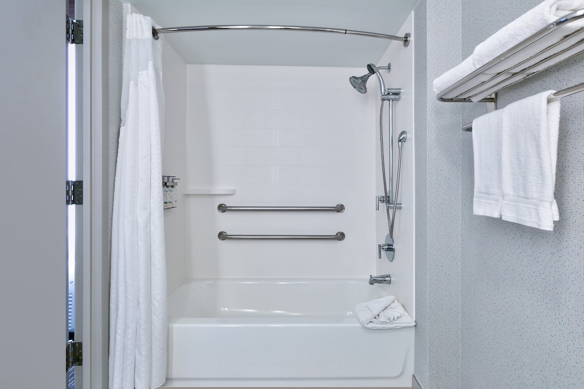A modern bathroom with a walk-in shower, grab bars, and a towel rack.